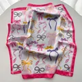 Detailed view of white silk scarf with pink borders and colorful bow patterns - Pink