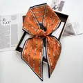 Detail van oranje en blauwe zijden twilly sjaal met kettingprint gestrikt in een geschenkdoos - Oranjerood