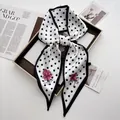 Detailed close-up of a white polka dot silk scarf tied in a bow with floral lotus print - White