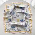 Detail view of silky square scarf featuring colorful bow prints and pearl patterns - Light Yellow