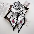 Polka dot silk scarf with pink flowers tied in a bow on a wooden tray for women - White