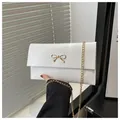 Close-up of white envelope bag featuring a gold bow ornament and delicate chain strap - White