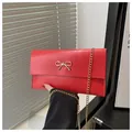 Detail of red envelope clutch bag with gold bow ornament and delicate chain strap - Red