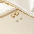 Detailed close-up of gold hoop earrings with white teardrop stones on cream silk fabric - White