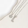 Macro detail of silver tone initial L pendants with cubic zirconia on textured background - Letter L / Silver