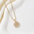Detailed close-up of golden letter O pendant with cubic zirconia on white silk - Letter O