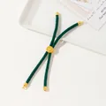 Detail of dark green woven bracelet with gold Tree of Life charm on a white tray - Green