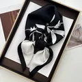 Eleganter Seidenschal mit schwarz-weißem Blumenmuster auf einem braunen Rahmen - Schwarz