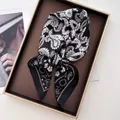 Détail d'un foulard en soie à motif paisley plié dans un coffret cadeau marron - Noir & Or