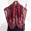 Close-up of burgundy square scarf with paisley and star prints on a wooden hanger - Red