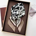 Dettaglio di un foulard in seta con stampa mucca e bordo marrone in un vassoio regalo - Bordo Caffè