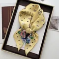 Élégant foulard en soie jaune à motif paisley floral posé sur un plateau avec revues - Jaune