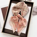 Dettaglio di sciarpa in seta a fiori e paisley annodata a fiocco su vassoio e rivista d'arte - arancio-rosso / Beige Rosso Arancio Paisley Floreale