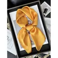 Carré de soie en satin doré avec un nœud élégant sur un fond de magazine minimaliste - Orange
