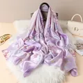 Detailed view of light purple floral silk scarf draped on a black leather handbag - Violet