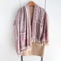 Bohemian paisley shawl with white tassels draped over a coat on a wooden hanger - Pink