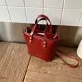 Sac seau bordeaux brillant avec détails dorés posé sur une surface en bois naturel - Rouge