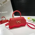 Sparkly red bow crossbody bag with wavy bottom and golden hardware on display - Red