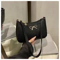 Nahaufnahme einer schwarzen Handtasche aus Leder mit goldener Schleife und Anhänger - Schwarz