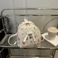 Mini cream backpack with pink cartoon prints and a decorative white leather bow charm - White
