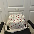 Cream corduroy shoulder bag with red strawberry print and adjustable strap in lifestyle setting - White