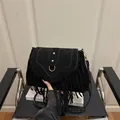 Retro black suede saddle bag with fringe details and gold rivets on a minimalist chair - Black