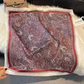 Flat lay of an elegant paisley silk scarf with warm red and cream tones on soft plush fabric - LQ-10
