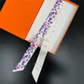 Detailansicht eines floralen langen Halstuchs auf einer orangefarbenen Luxus-Geschenkbox - 5x120cm / Violett Weiß