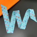 Detail eines hellblauen Seidenschals mit bunten Herzmustern und orangefarbener Box - Hellblau