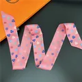 Makro-Detail eines rosa Seidenschals mit Herzmuster und oranger Geschenkbox - Rosa