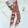 Detail of elegant orange chain print skinny scarf laid flat with lifestyle accessories - Orange