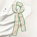 Detail of elegant floral silk scarf with green edges over white satin fabric - Cream Floral Style