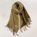 Detalle de la textura de bufanda de cachemira caqui con borlas y etiqueta tejida - Khaki and Camel