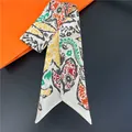 Detail of a paisley print skinny silk scarf displayed near a luxury orange gift box - Pattern 2 (White Paisley)