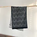 Detail view of double-sided geometric cashmere scarf with delicate short fringes on wood - 185x65cm / Black & White