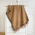 Detail of coffee cashmere scarf showing clover pattern and long tassel fringes on white cabinet - Khaki