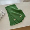 Detail showing the green knitted wool scarf texture with material label and ribbed edge - Green