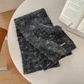 Detail of soft charcoal grey knitted scarf with leather VEGETABLE tag on a white table - 170x26cm / Black