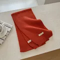 Detailed view of the 70% wool blend fabric and product label on a rust orange scarf - Orange