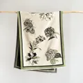 Detail eines Blumen-Jacquard-Schals mit grünem Rand und feinen Fransen am Holzzweig - Beige und Grün