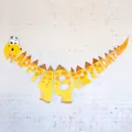 Close-up of a yellow dinosaur HAPPY BIRTHDAY banner with orange spots for party decor - Yellow Dinosaur Theme