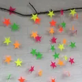 Close-up of neon fluorescent star paper garland hanging on a rustic wooden branch - Luminous Star