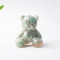 Dettaglio ravvicinato di una statuetta a orso in resina con cristalli verdi e base oro - Amazzonite
