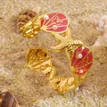 Detail van een gouden armband met zeester en schelp op een achtergrond van zand - Rood