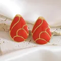 Macro shot of red enamel teardrop earrings with gold metal frame on a marble texture - Red