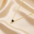 Close-up of heart-shaped black stone pendant with gold chain on champagne silk - Black