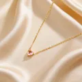 Detail einer rosa Herz-Geburtsstein-Halskette mit Goldkette auf beigem Satinhintergrund - Rosa