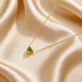 Nahaufnahme des herzförmigen grünen Edelsteinanhängers an einer Goldkette auf Seide - Grün