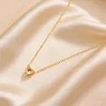 Detailed close-up of golden heart necklace with pink stone on champagne satin - Champagne