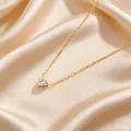 Makroansicht eines herzförmigen Edelsteinanhängers mit Goldkette auf champagnerfarbener Seide - Weiß